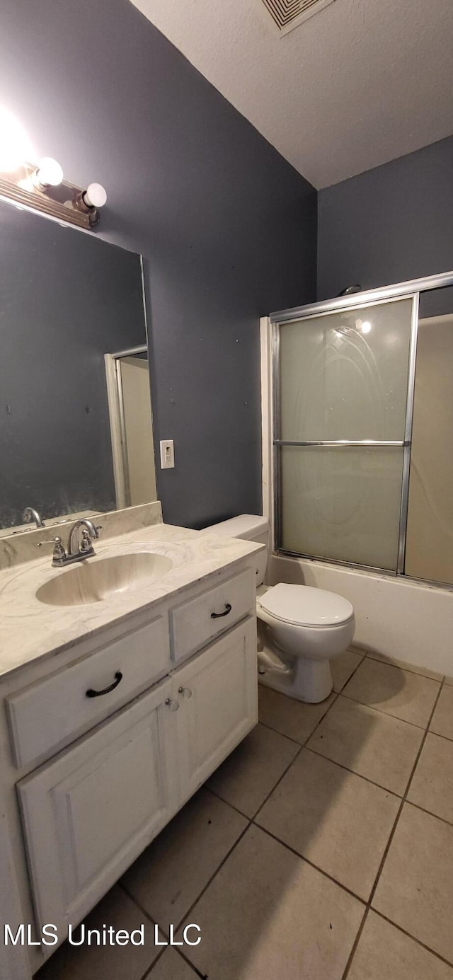 full bathroom featuring toilet, a textured ceiling, bath / shower combo with glass door, tile patterned flooring, and vanity