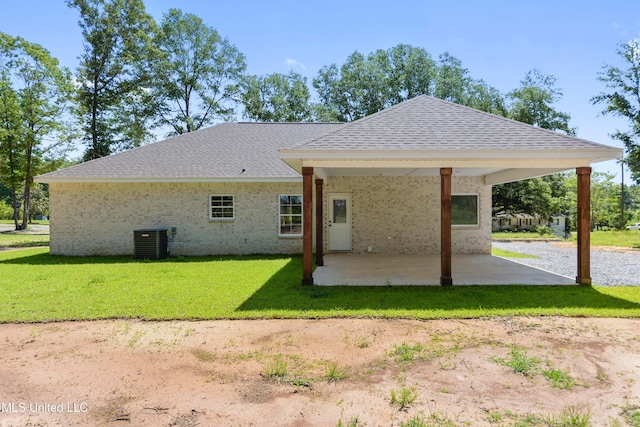 rear view of house featuring roof with shingles, a patio area, brick siding, central AC unit, and a yard