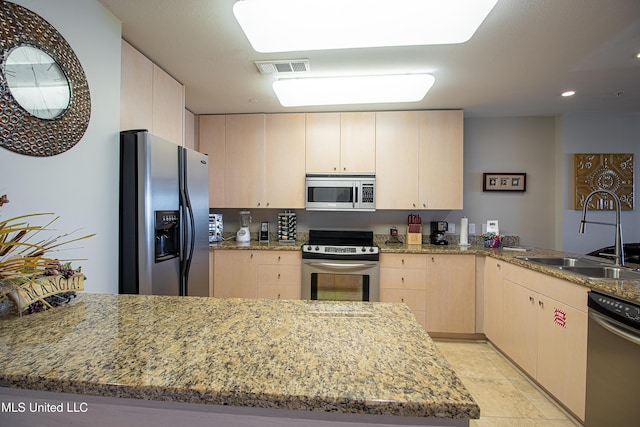 kitchen with light brown cabinetry, a peninsula, stainless steel appliances, and a sink