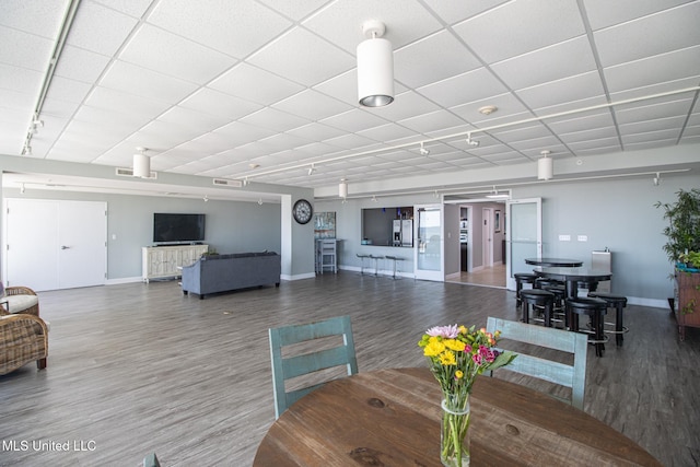 dining area with a paneled ceiling, baseboards, wood finished floors, and track lighting