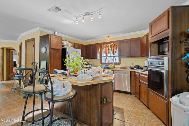 kitchen featuring light tile patterned floors, a kitchen breakfast bar, a textured ceiling, ornamental molding, and black appliances