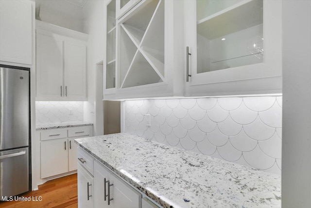 kitchen with backsplash, light wood-type flooring, white cabinets, light stone counters, and stainless steel refrigerator