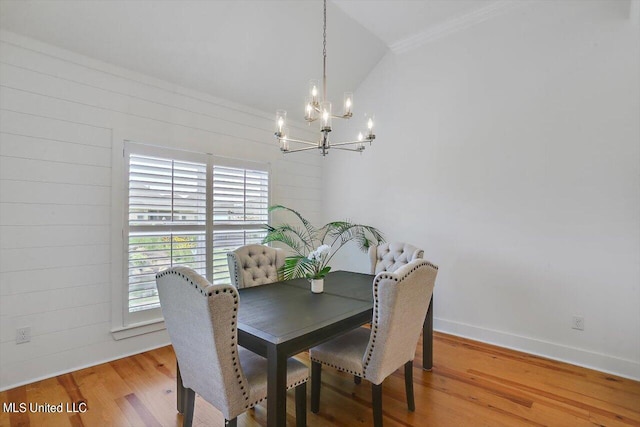 dining area with light hardwood / wood-style floors, vaulted ceiling, wooden walls, a notable chandelier, and ornamental molding