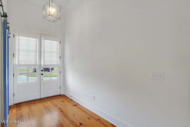 entryway featuring french doors, light hardwood / wood-style flooring, a notable chandelier, and a barn door