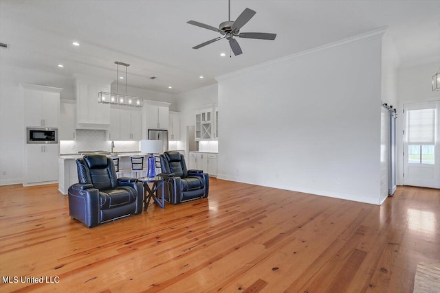 living room featuring ceiling fan, ornamental molding, and light wood-type flooring