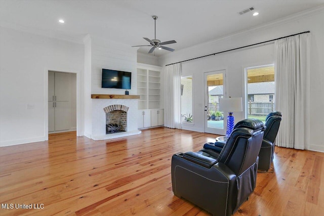 living room featuring crown molding, a brick fireplace, light hardwood / wood-style floors, and ceiling fan