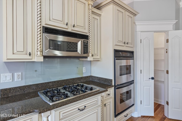 kitchen with dark stone counters, stainless steel appliances, crown molding, cream cabinets, and light hardwood / wood-style flooring