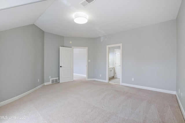 unfurnished bedroom featuring ensuite bathroom, lofted ceiling, and light colored carpet