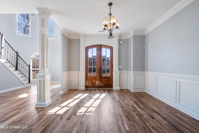 foyer entrance with decorative columns, ornamental molding, wood-type flooring, and french doors