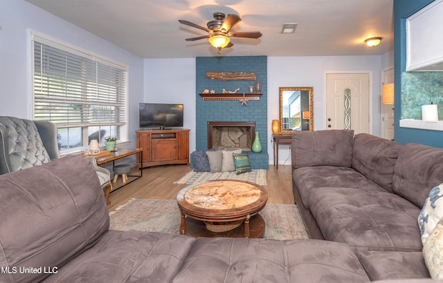 living room featuring ceiling fan, light wood-type flooring, and a fireplace