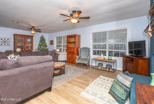 living room with a textured ceiling, light wood-type flooring, and ceiling fan