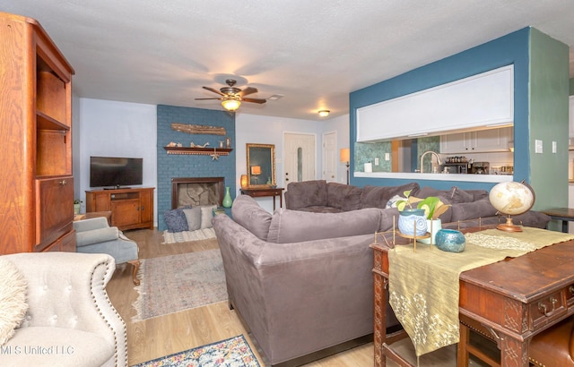 living room featuring a brick fireplace, light hardwood / wood-style flooring, ceiling fan, and sink