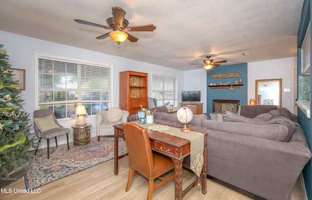 living room featuring a fireplace, a textured ceiling, light wood-type flooring, and ceiling fan