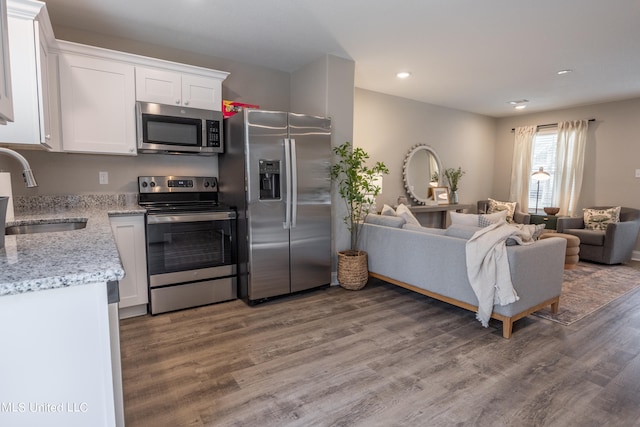 kitchen with stainless steel appliances, hardwood / wood-style floors, sink, white cabinetry, and light stone counters