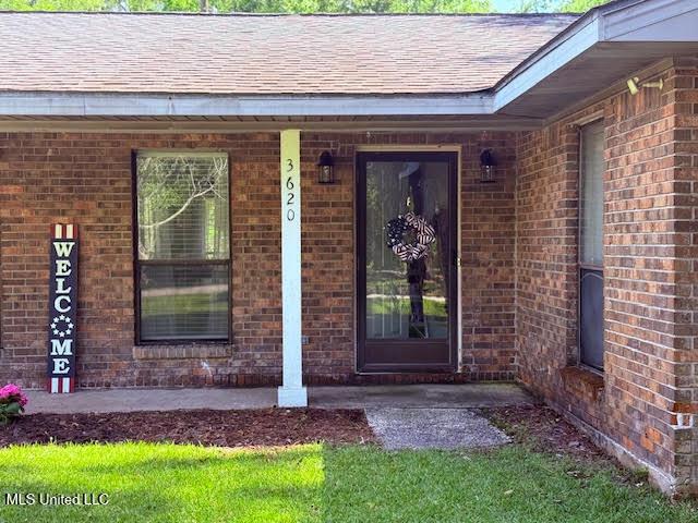 3620 Cochran Ave, Moss Point, MS 39562 - doorway to property featuring brick siding, a shingled roof, and covered porch