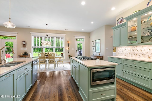 kitchen with a sink, backsplash, green cabinets, appliances with stainless steel finishes, and hanging light fixtures
