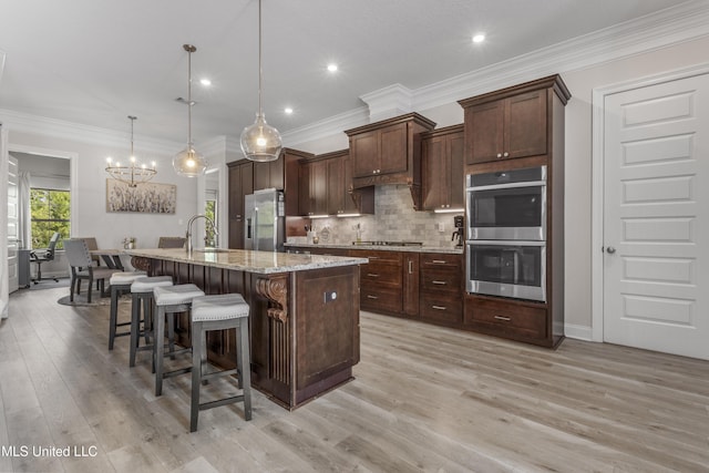 5705 Via Toscana, Ocean Springs, MS 39564 - kitchen featuring stainless steel appliances, a center island with sink, a chandelier, a kitchen breakfast bar, and backsplash
