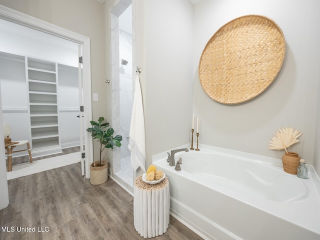 full bathroom with a garden tub, wood finished floors, a walk in closet, and a shower stall