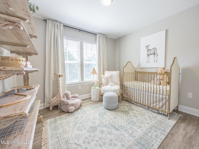 bedroom with a nursery area, baseboards, and wood finished floors