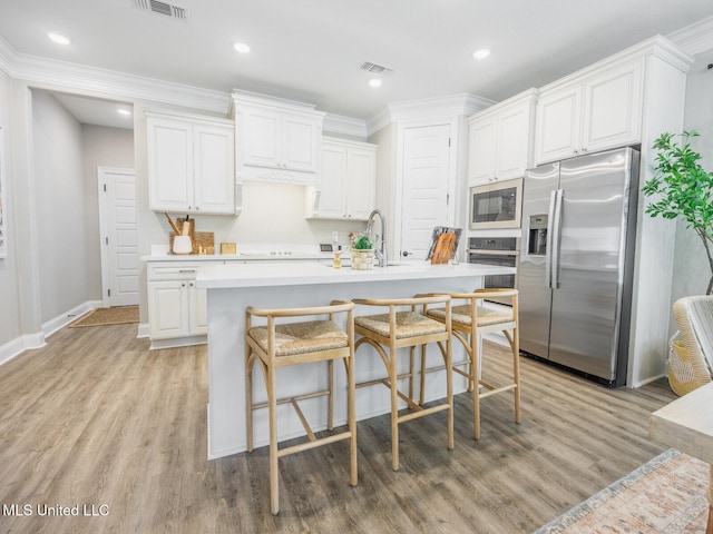 kitchen with appliances with stainless steel finishes, light countertops, white cabinets, and a center island with sink