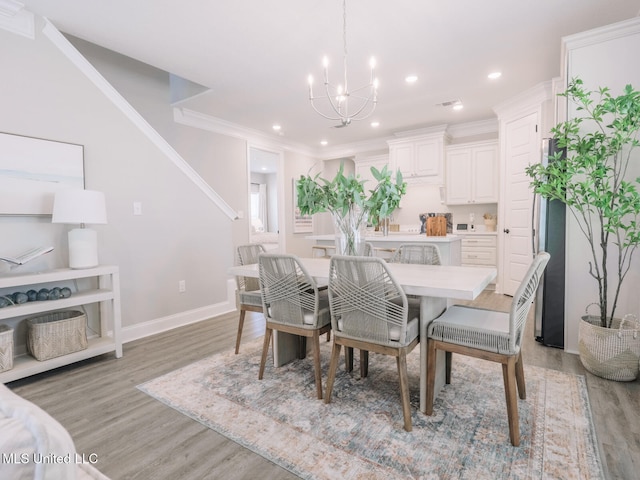 dining area featuring a notable chandelier, ornamental molding, and light wood-style floors