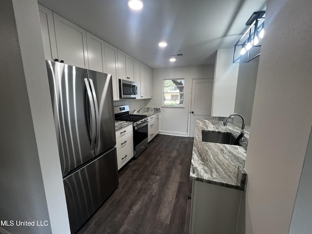 kitchen featuring appliances with stainless steel finishes, sink, white cabinets, light stone countertops, and dark wood-type flooring