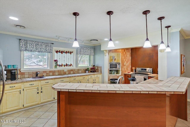 kitchen with light tile patterned flooring, stainless steel appliances, ornamental molding, backsplash, and tile counters