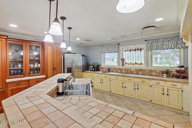 kitchen with tile counters, ornamental molding, sink, stainless steel fridge with ice dispenser, and pendant lighting