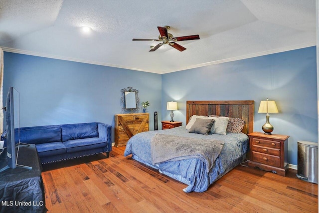 bedroom featuring a textured ceiling, ornamental molding, wood-type flooring, and a ceiling fan