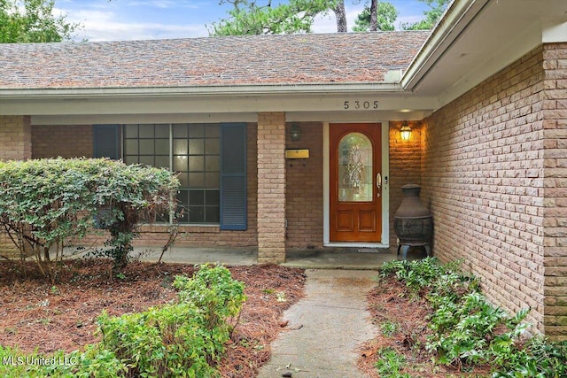 doorway to property featuring brick siding, a porch, and a shingled roof