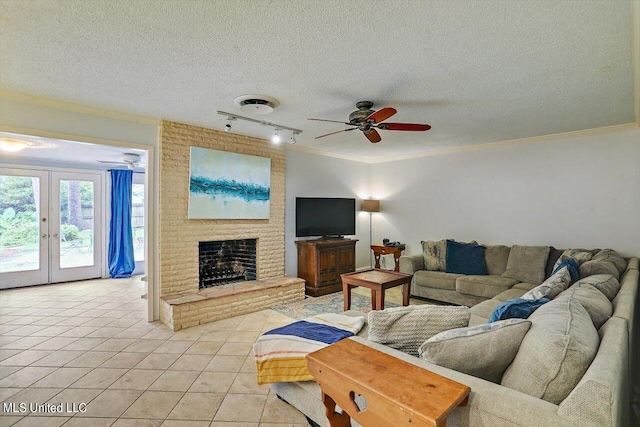 living room featuring ceiling fan, light tile patterned floors, a textured ceiling, a brick fireplace, and ornamental molding