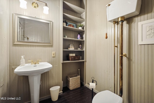 bathroom featuring hardwood / wood-style floors, wood walls, toilet, and a sink