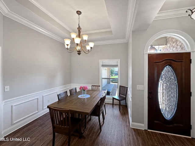 dining area with wainscoting, a raised ceiling, an inviting chandelier, ornamental molding, and dark wood-type flooring
