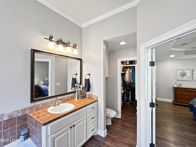 ensuite bathroom with crown molding, wood finished floors, vanity, baseboards, and ensuite bath