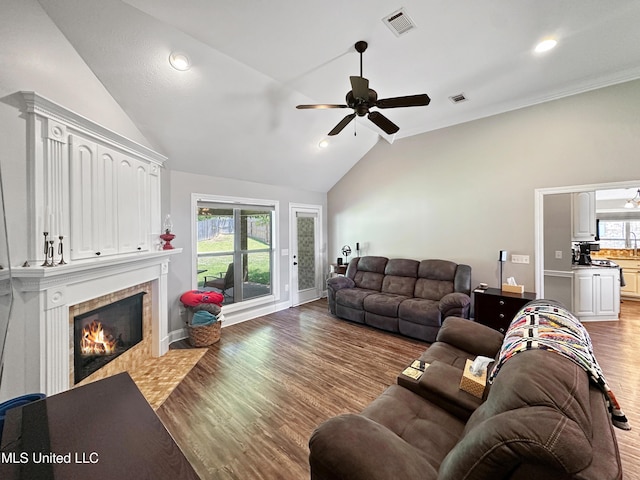 living room featuring ceiling fan, visible vents, vaulted ceiling, a tile fireplace, and wood finished floors