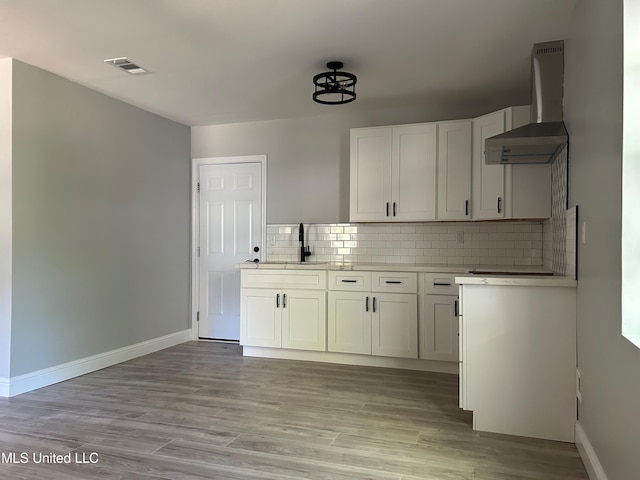 kitchen with tasteful backsplash, extractor fan, sink, light hardwood / wood-style flooring, and white cabinets