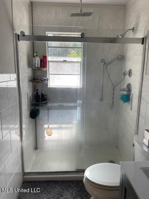 bathroom with vanity, a shower with shower door, tile walls, and toilet