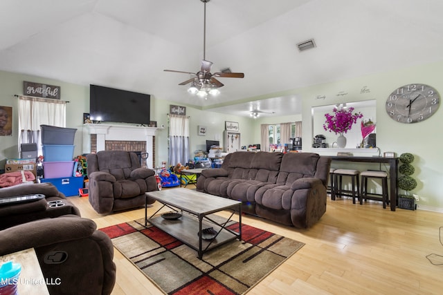 living room with ceiling fan, vaulted ceiling, light hardwood / wood-style floors, and a fireplace