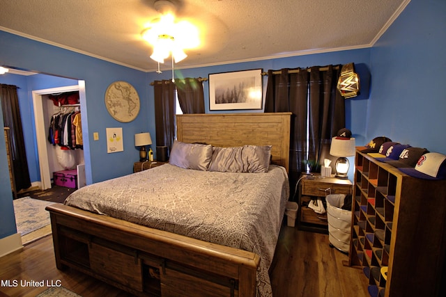 bedroom with a walk in closet, a textured ceiling, dark hardwood / wood-style flooring, a closet, and ornamental molding