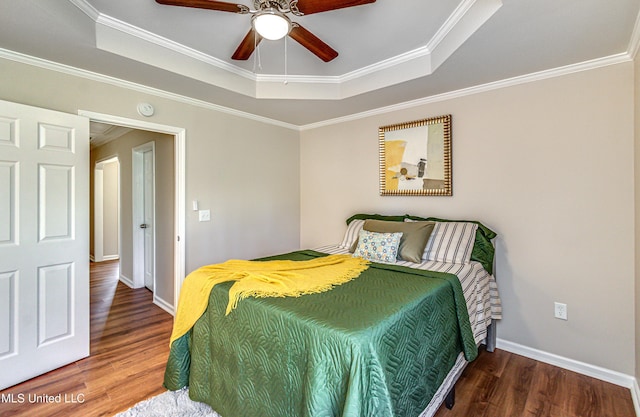 bedroom featuring a raised ceiling, wood finished floors, baseboards, and ornamental molding