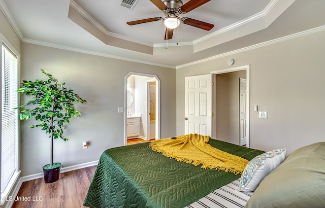 bedroom featuring wood finished floors, baseboards, arched walkways, ornamental molding, and a raised ceiling