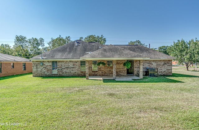 rear view of house with a patio, a lawn, brick siding, and roof with shingles