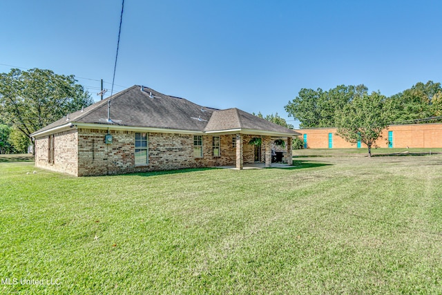 rear view of house featuring a patio, a lawn, brick siding, and a shingled roof