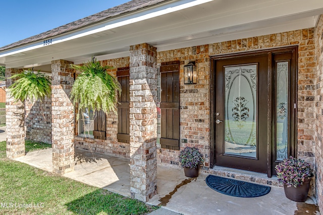 doorway to property featuring a porch and brick siding