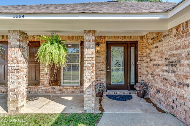 property entrance featuring brick siding, roof with shingles, and covered porch