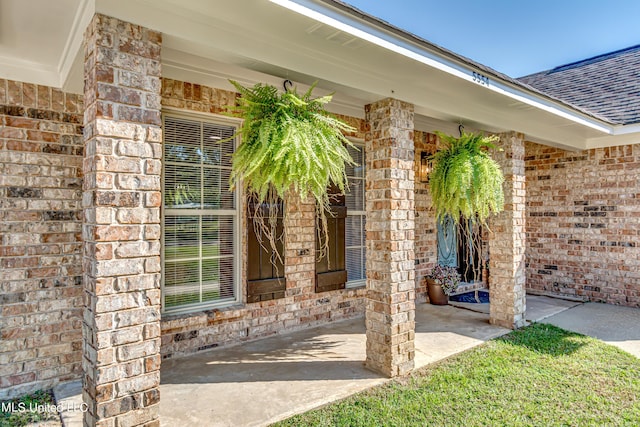 property entrance featuring covered porch, brick siding, and a shingled roof