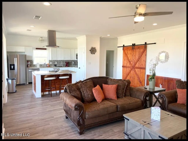 living room with crown molding, a barn door, light hardwood / wood-style floors, and ceiling fan