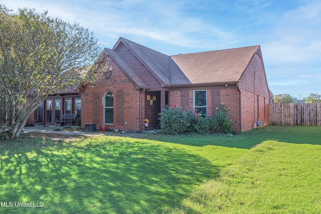 view of front of home with a front yard, brick siding, fence, and roof with shingles