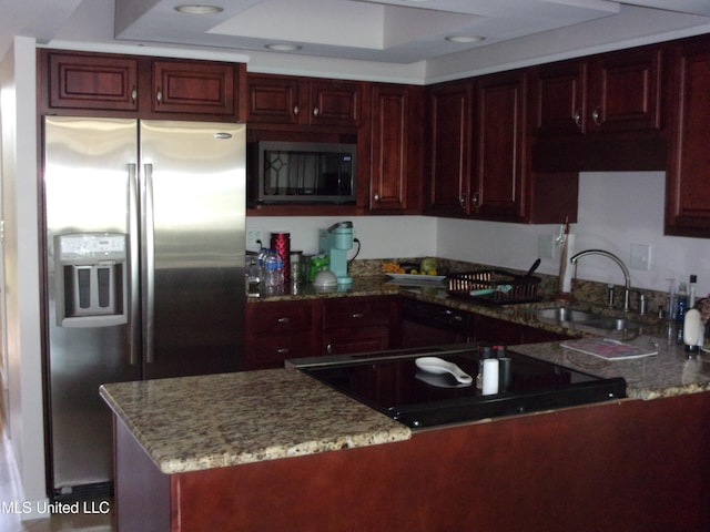 kitchen with kitchen peninsula, stainless steel appliances, sink, light stone countertops, and a raised ceiling