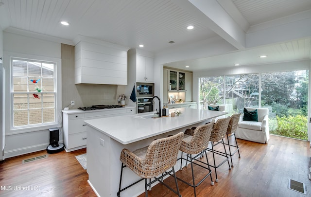 kitchen with built in microwave, gas cooktop, white cabinets, and a center island with sink